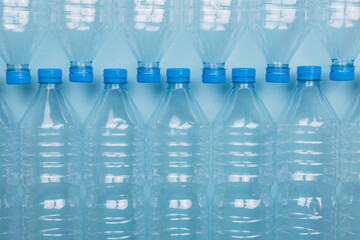 Empty clear plastic bottles with caps stacked on a blue background. Recycling and environment concept.