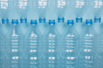 Empty clear plastic bottles without caps stacked on a blue background. Recycling and environment concept.