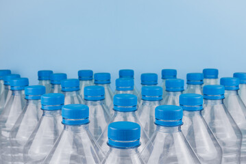 Empty clear plastic bottles with caps stacked on a blue background. Recycling and environment concept.