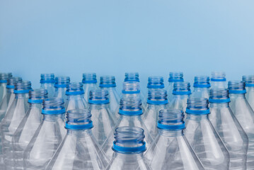 Empty clear plastic bottles without caps stacked on a blue background. Recycling and environment concept.
