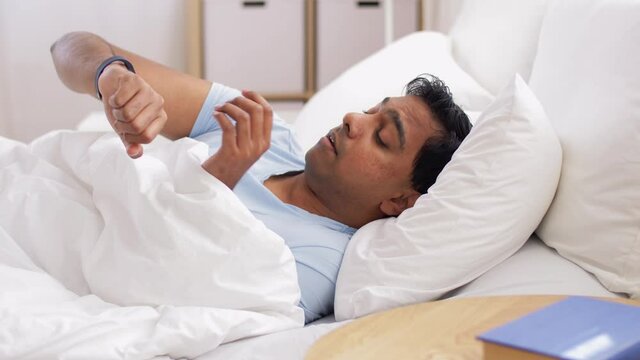 people, bedtime and rest concept - sleeping indian man with health tracker awaking in bed at home