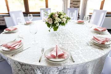 Festive table setting with wine glasses, and fresh flowers. Selebration banquet with pink napkins, white plates and wineglasses in restaurant