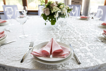 Close up festive table setting with empty wineglasses. Selebration banquet with white plates, pink napkin and wineglasses for white and red wine on the lace white table in restaurant