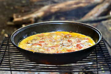 Blur. Fried eggs with vegetables are cooked in a pan on a grill on coals in the open air.