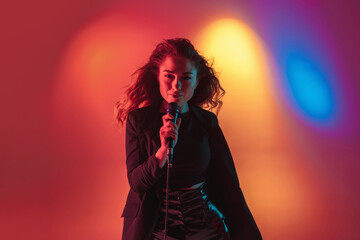 Dancing. Young caucasian inspired and expressive musician, female singer performing on multicolored background in neon. Concept of music, hobby, festival, art. Joyful artist, colorful, bright portrait