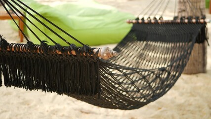 Black hammock stretching between coconut palms. Mesh vintage hipster hammock with fringe on edges stretched on sandy paradise beach of tropical island. Relax, travel vacation holiday resort concept.