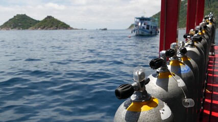 Row of oxygen tanks and diving equipment placed on modern boat in rippling ocean near Koh Tao...