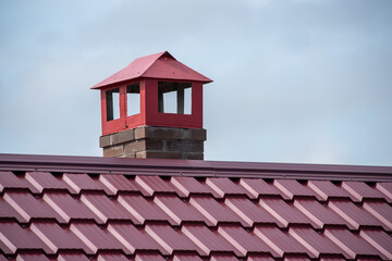 House roof with modern red metal tiles and chimney close up
