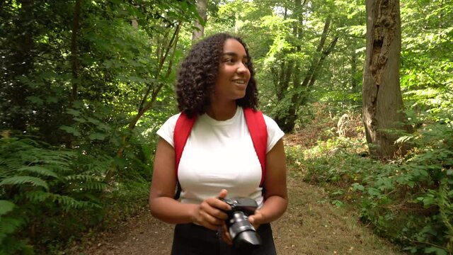 Teenage girl young woman hiking with red backpack and taking photographs with a camera in forest woodland 