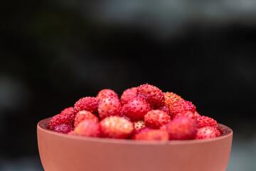 A clay cup with red, juicy strawberries stands on a wooden table