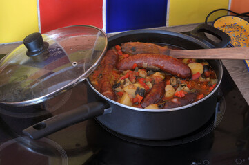 Ratatouille et saucisses cuisant dans une poêle sur une table de cuisson