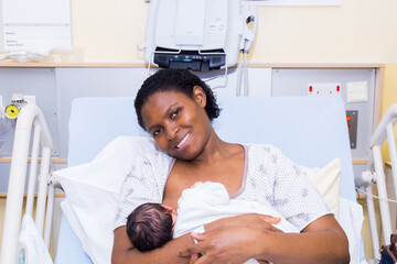 Black mother and  new born child in hospital, smiling and breastfeeding.