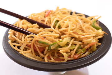 Schezwan Noodles or vegetable Hakka Noodles or chow mein is a popular Indo-Chinese recipes, served in a bowl or plate with wooden chopsticks. 