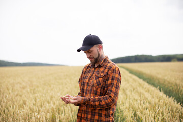 Naklejka na ściany i meble A farmer in a checkered orange shirt stands in a wheat field
