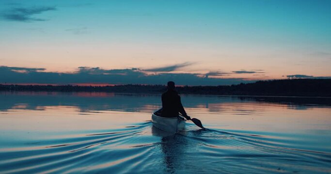 Man canoeing in a traditional wooden boat on a large lake at dawn. Shot on RED cinema camera with 2x anamorphic lens