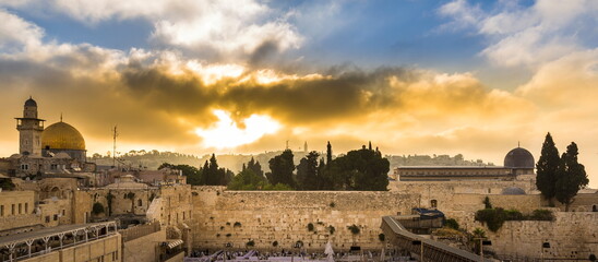 Obraz premium Beautiful sunrise clouds over the Mount of Olives and the Temple Mount sites: Dome of the Rock, Western Wall and Al Aqsa Mosque; with Jewish people praying in sections because of covid-19 regulations 