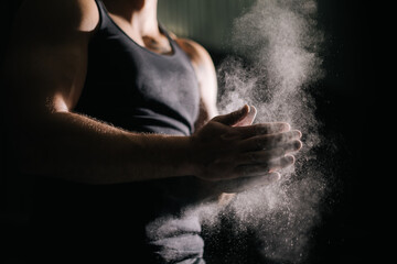 Close-up of unrecognizable muscular man clapping hands with talc and preparing for workout at gym. Closeup of strong male hands preparing for fit workout in gym with chalk magnesium carbonate. - obrazy, fototapety, plakaty