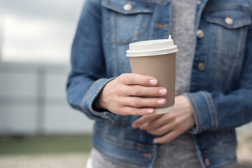 Women's hands with pink manicure in a denim jacket hold a Cup of coffee to go, zero west