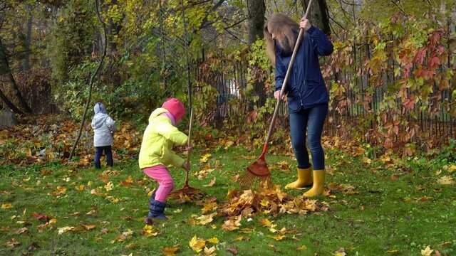 Little daughter girl helping her mother with leaves raking in garden