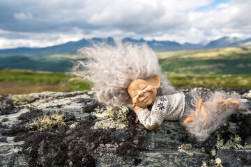 Beautiful peaceful and sleeping troll girl figure relaxing outdoors with mountain scenery in the background. - obrazy, fototapety, plakaty