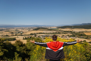 Naklejka na ściany i meble Happy young traveler spreading arms in mountains background.Happy man standing arms stretched back and enjoy life on the hill