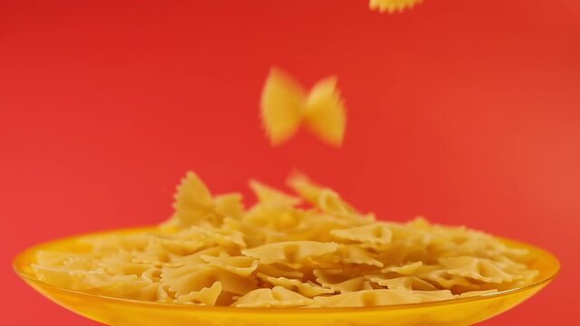 Falling raw italian farfalle pasta on red color background with copy space, 4K UHD video footage