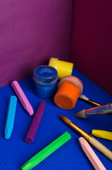 Vertical image.Closeup of colorful crayons, gouache, brushes on the blue and purple background