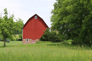 bright red farm barn with fresh painted white trim in a natural field with trees and agriculture beyond