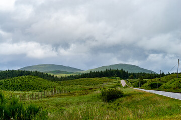 Photography of Scottish highlands with a road leading into the horizon with mountains in the background under a cloudy sky.