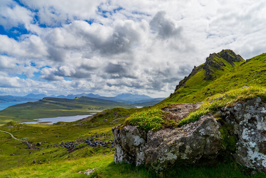 Landscape photography of Scottish Highlands from Isle of Skye with sea and Scottish mountains in the background under a cloudy sky with a rock in the first plan.