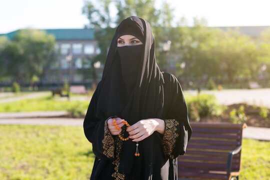 A woman from the east in national Islamic clothes holds religious supplies in her hands.