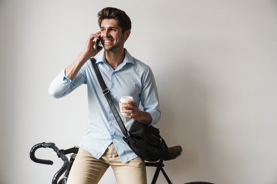 Image of happy man holding coffee and talking on cellphone by bicycle