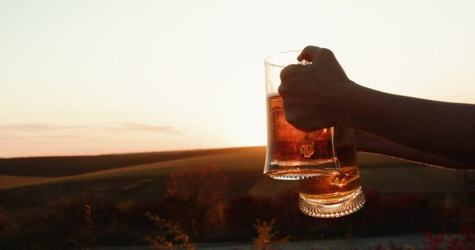 Female hands holds two pints of beer on sun shining on colourful nature