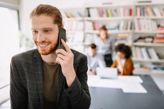 Happy young man using mobile phone and smiling while his colleagues working in office