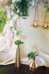 Wedding decoration, floristry.Succulents in gold vessels near the table with a light tablecloth.