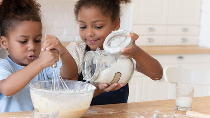 Cute little african american brother and sister kids have fun preparing dough for cookies or pie in...