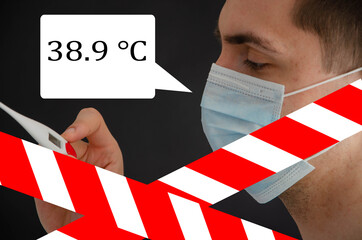A man in a blue medical mask on a black background looks at a thermometer and next to it is a dialog box for text.  Copy Space