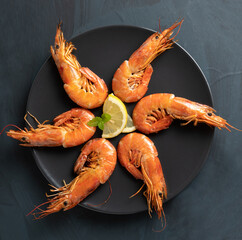 Grilled prawns on a black dish, on a rustic wooden table, top view