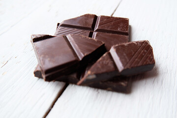 Dark chocolate bar top view mock up with space for text close up. Broken pieces of dark chocolate macro, mock-up for design. Food background over white wooden table.