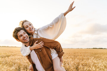 Image of young caucasian couple doing piggyback ride in golden field