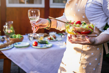 Woman holding wineglass with white wine and vegetable salad outdoors. Preparing food and refreshment for buffet