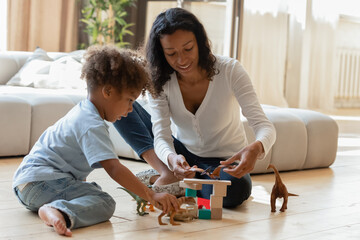 Playful young african American mother sit on floor in living room play toys with little son, loving biracial mom nanny engaged in funny activity game with animals blocks with small boy child at home