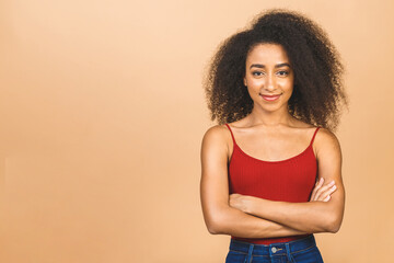 Portrait of beautiful positive african american black woman standing with arms crossed isolated over beige background.
