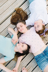Obraz na płótnie Canvas three girls lie with closed eyes on a wooden pier. rest, picnic
