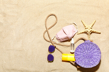 Beach accessories and protective mask on sand background. Vacation during epidemic