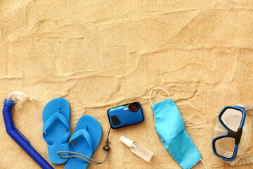 Beach accessories and protective mask on sand background. Vacation during epidemic