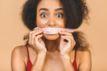 Dieting concept. Slim shocked amazed african american woman shows centimeter isolated over beige background.