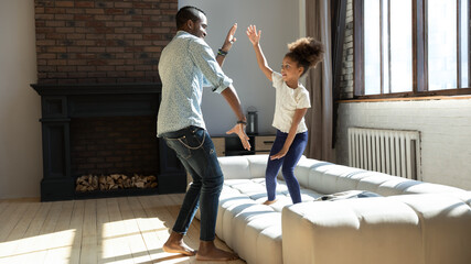 Overjoyed young african american dad have fun with happy little daughter in living room, playful biracial father and small girl child play engaged in funny activity at home, enjoy family weekend