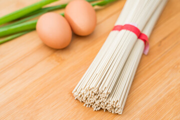 Dried noodles, eggs and chives on the chopping board