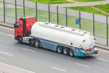 Heavy truck with a tank for flammable liquids rides on the road, back view.